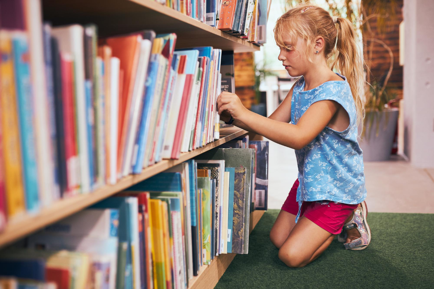 Una niña pequeña examina libros en una gran estantería, en el entorno de una biblioteca.