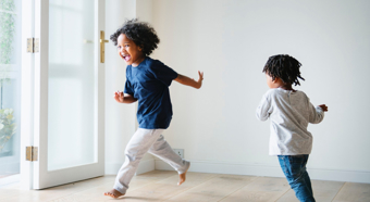 Dos niños pequeños en un entorno hogareño luminoso jugando a perseguirse y riendo.