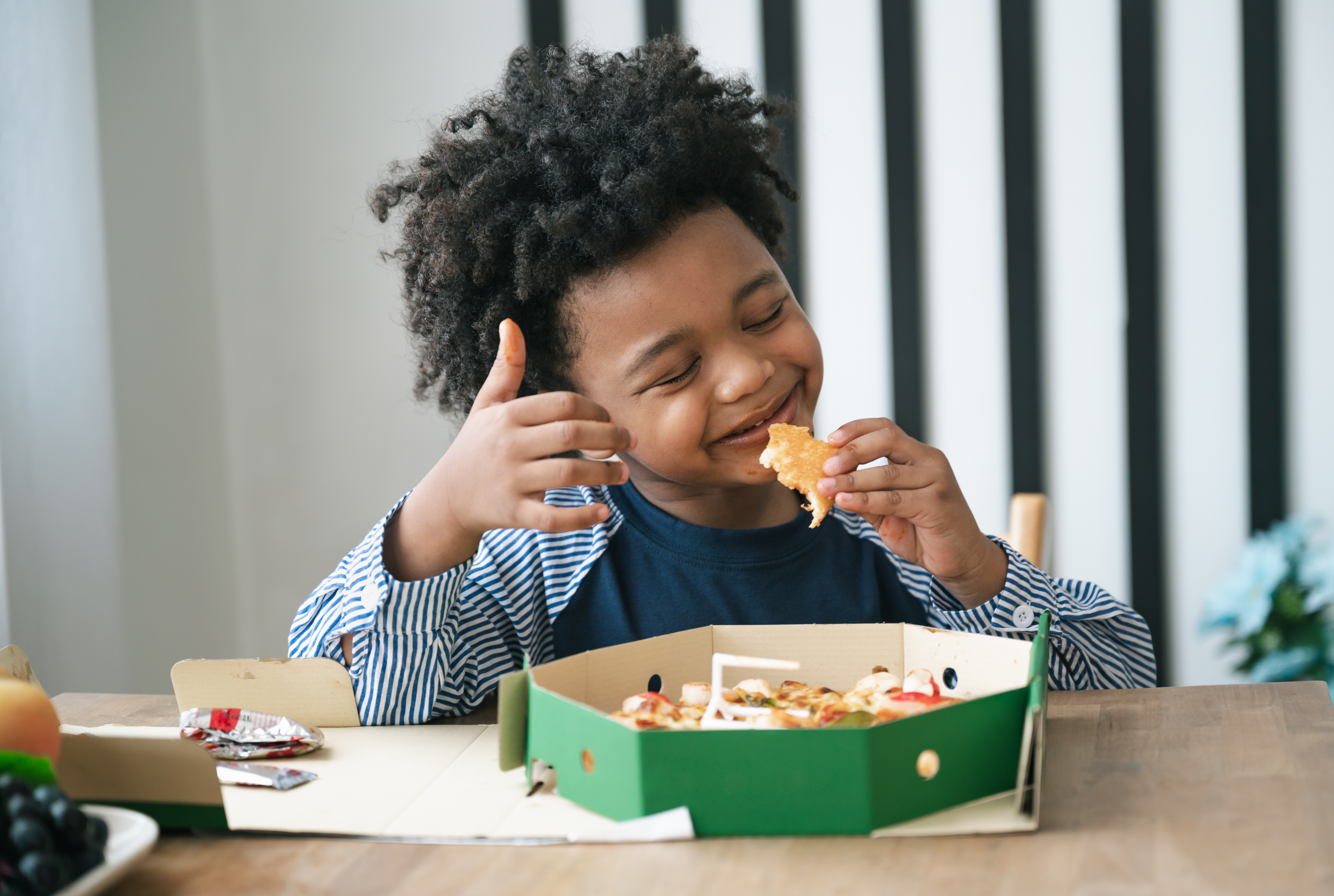 Niño comiendo en una mesa con una gran sonrisa en su cara.