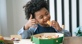 Niño comiendo en una mesa con una gran sonrisa en su cara.