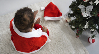 Bebé jugando adentro con traje de Papá Noel junto al árbol de Navidad, ángulo alto