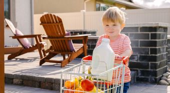 Un niño pequeño que viste una camisa de rayas naranjas empuja un mini carrito de compras con frutas y un gran recipiente de leche.