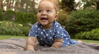 Bebé sonriente arrastrándose sobre una manta, con un bonito telón de fondo de naturaleza verde.