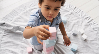 Primer plano de un niño pequeño apilando pequeños bloques en un cómodo entorno hogareño.