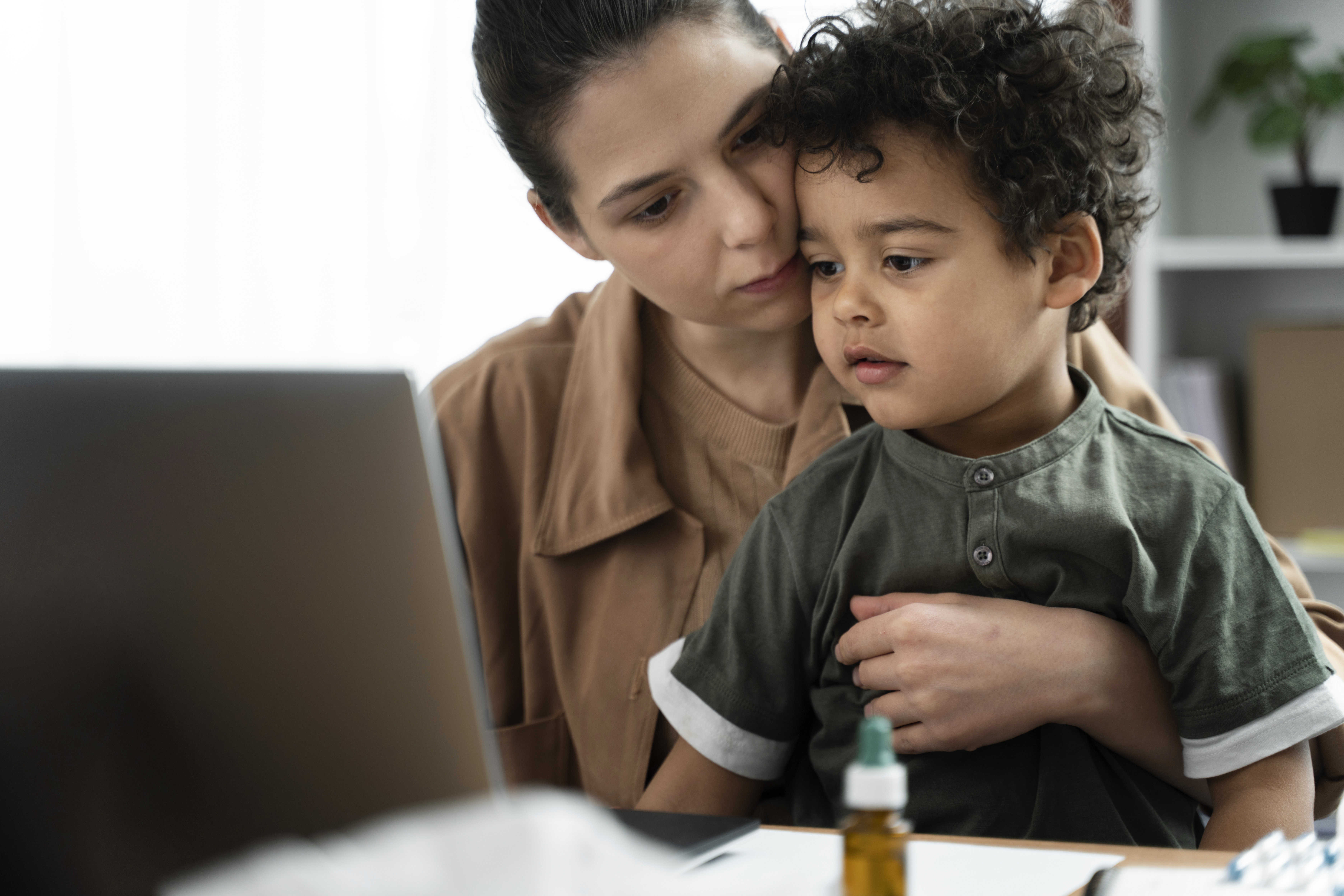 Una mujer sostiene en su regazo a un niño con una camisa verde oscuro, mientras ambos miran la pantalla de una computadora portátil