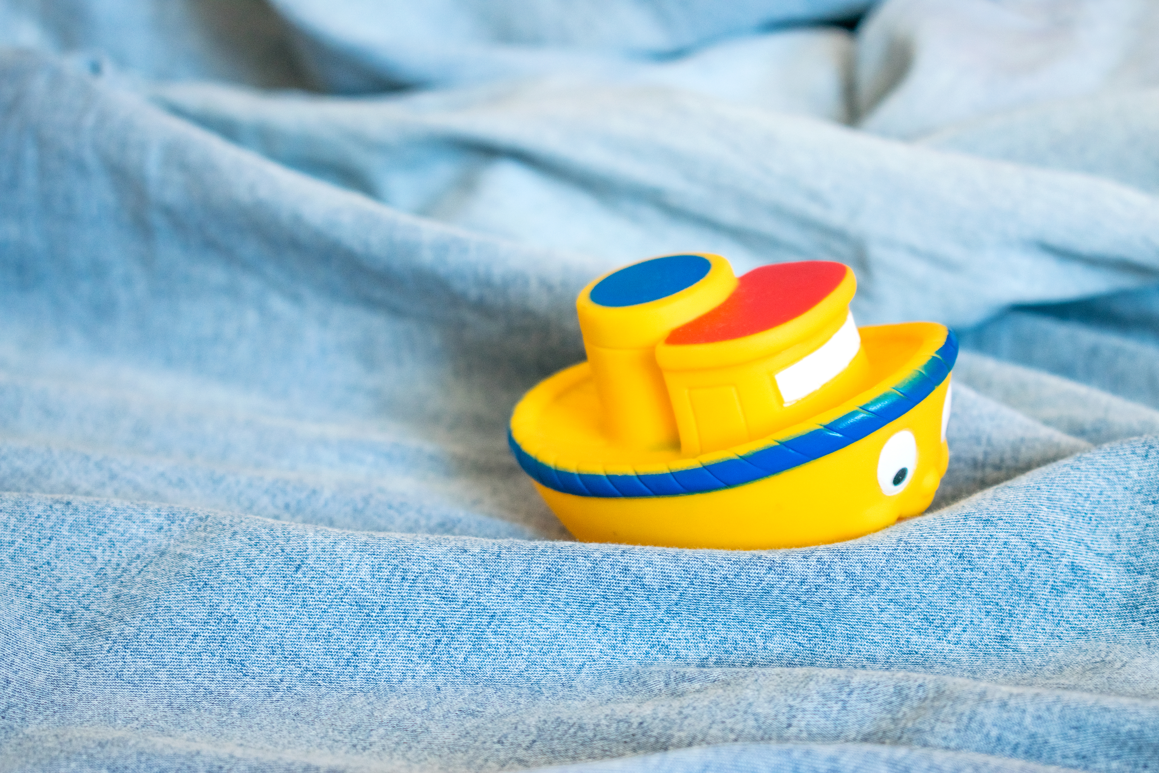 Un pequeño barco de juguete amarillo sobre un denim claro lavado, parece un pequeño barco en el agua.